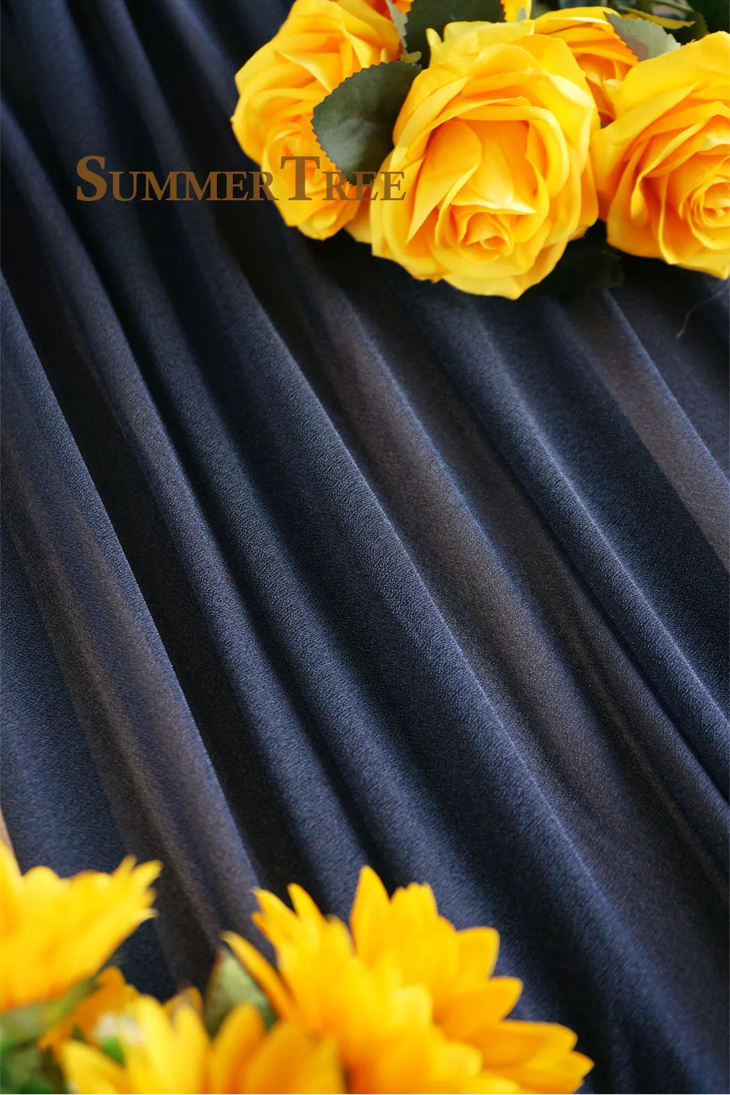 A close-up of bright yellow roses and sunflowers arranged against a dark blue draped fabric.