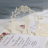 A white laser cut archway decoration for a wedding invitation featuring gold pearls and floral elements.