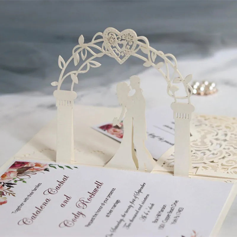 A white laser cut archway decoration for a wedding invitation featuring gold pearls and floral elements.