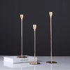 A set of three slender gold-toned iron candle holders displayed on a white book against a dark background.