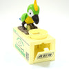 A plastic parrot bird figurine sitting on a yellow money bank box.