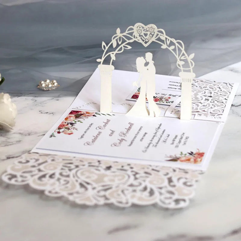 Gold pearl laser cut wedding invitations featuring a white arch and silhouette of a couple on a marble surface