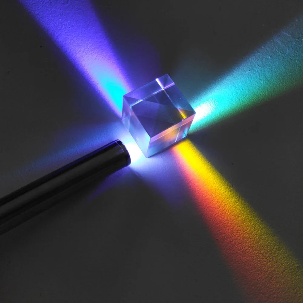 A clear crystal prism cube is illuminated, casting a vibrant rainbow spectrum onto a dark surface.