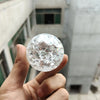 A hand holds a clear, spherical crystal ball water feature ornament against a blurred architectural background.