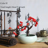 Artificial silk cherry blossom branches in red and pink on a dark branch set in a white ceramic pot