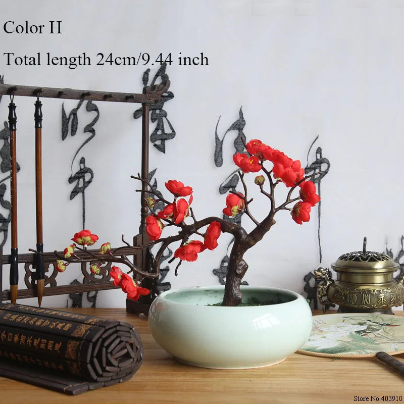 Artificial silk cherry blossom branches in red and pink on a dark branch set in a white ceramic pot