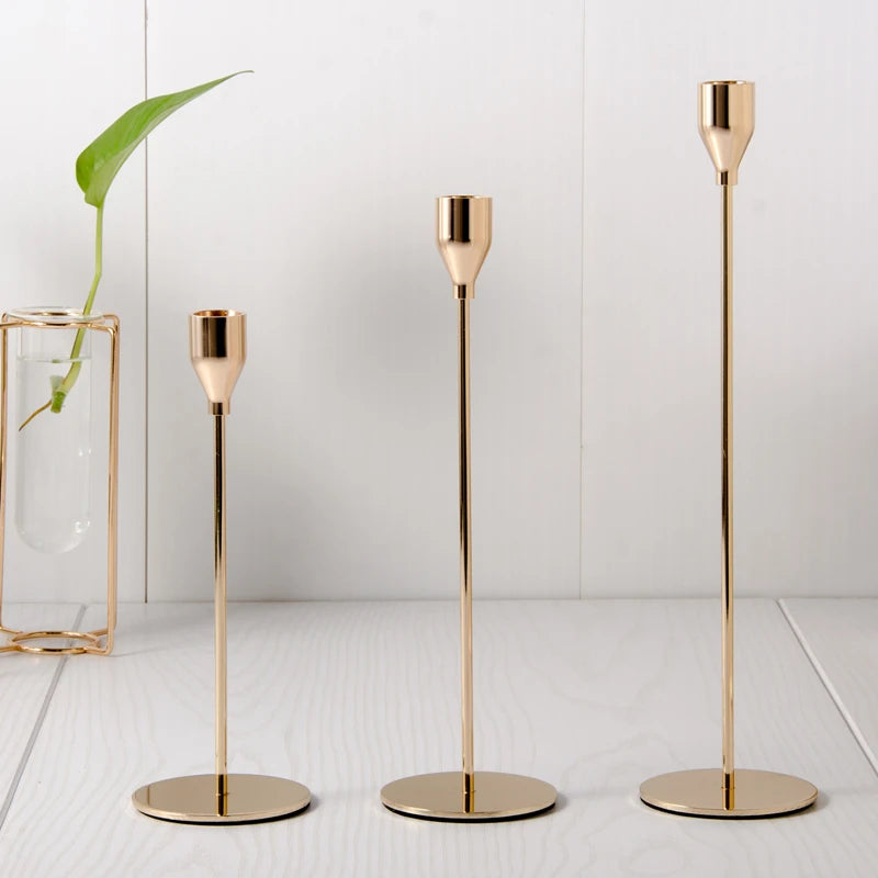 Three slender gold-toned iron candle holders standing on a white surface.