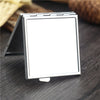 A silver mini double-sided folding makeup mirror is shown open on a dark wooden surface.