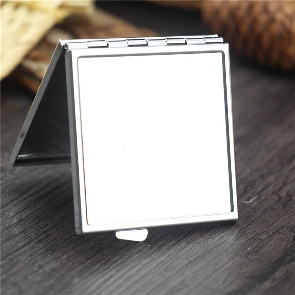 A silver mini double-sided folding makeup mirror is shown open on a dark wooden surface.