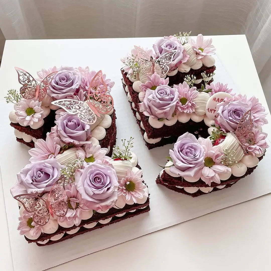 A set of purple and pink floral cake toppers featuring gold butterfly accents on dark chocolate cakes.