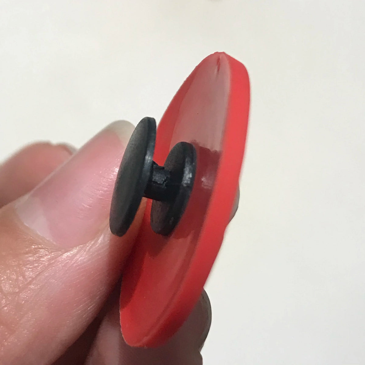 A close-up of a red PVC shoe charm with a black dinosaur-shaped clip being held by a finger.
