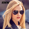 A blonde woman wearing classic pilot sunglasses with mirror lenses outdoors.