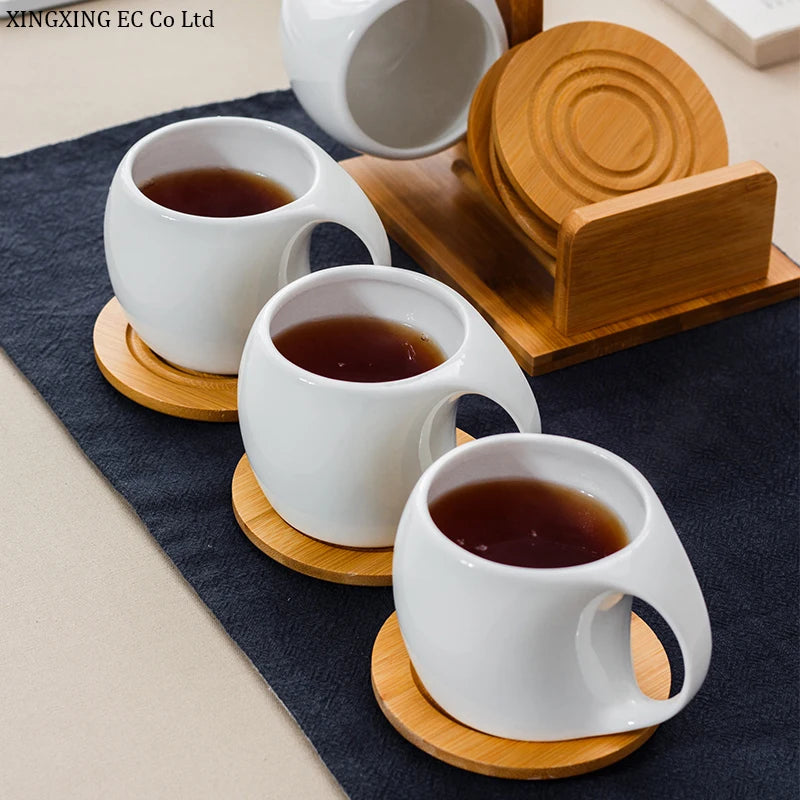 A set of white ceramic coffee mugs filled with dark liquid, resting on individual bamboo wood stands.