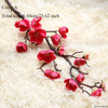 A branch of artificial silk cherry blossoms with vibrant red and pink flowers on a light background.