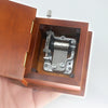 A close-up view of a wooden music box with an open lid revealing a metal hand-crank mechanism inside.
