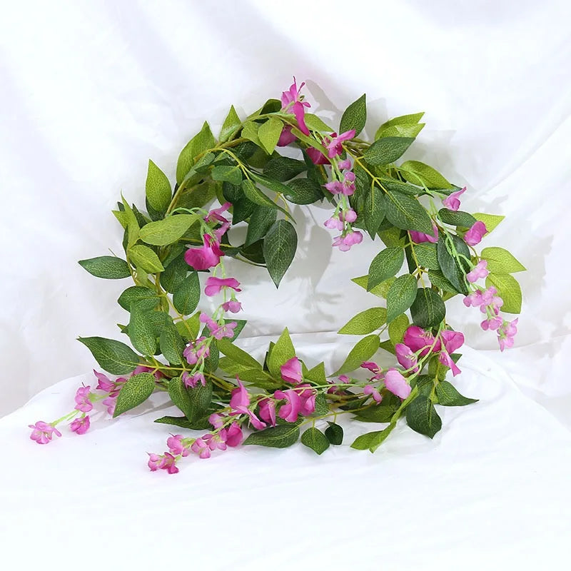 A green silk wisteria garland vine with pink flowers used for weddings and home decor.