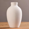 A white ceramic vase with vertical ribbing sits on a wooden surface.
