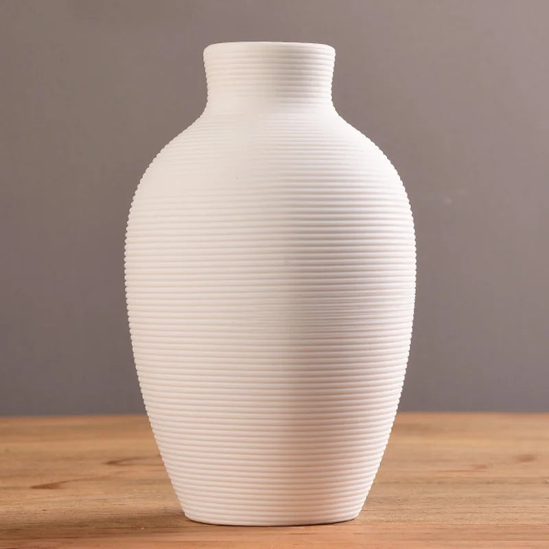 A white ceramic vase with vertical ribbing sits on a wooden surface.