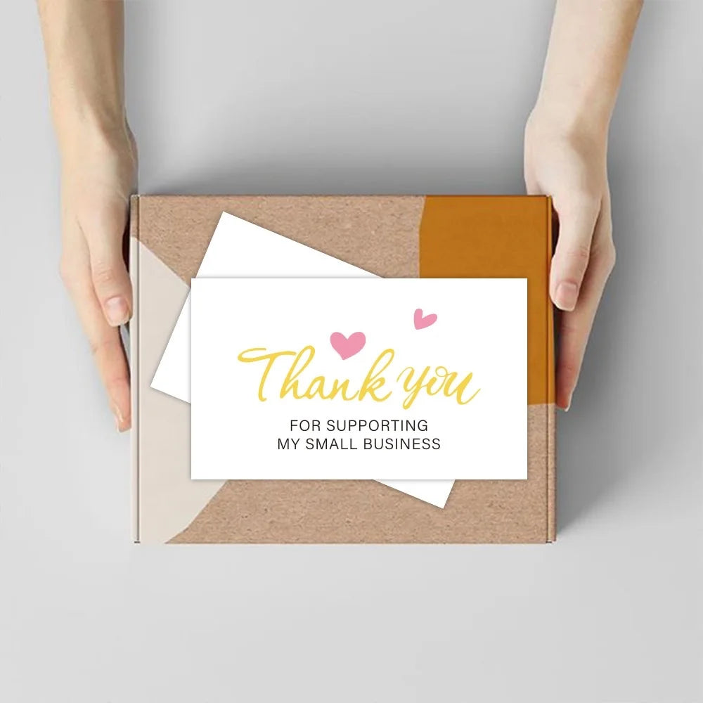 Hands holding a kraft paper box containing white thank you cards for supporting a small business
