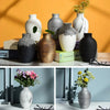 A collection of modern ceramic flower vases in various shades of gray, black, and white displayed against an orange wall.