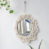 Boho macrame round wall mirror with a textured fringe frame hanging on a white wall.