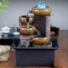 A tabletop water fountain featuring stacked, earthy-toned ceramic bowls and a blue glass sphere.