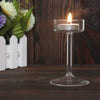 Elegant glass candle holder with a lit white candle on a dark wooden surface.