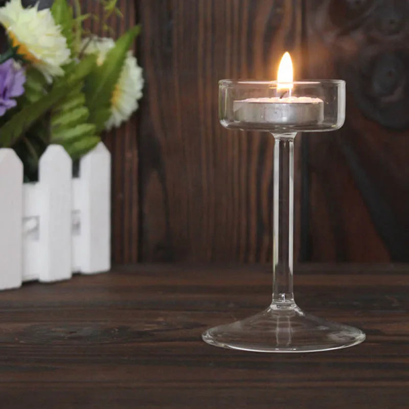 Elegant glass candle holder with a lit white candle on a dark wooden surface.