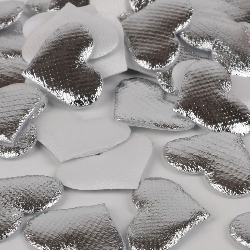 Silver heart-shaped sponge confetti scattered on a white surface.