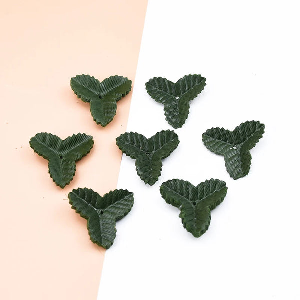A collection of small, artificial green leaves shaped like hearts scattered on a light pink and white background.