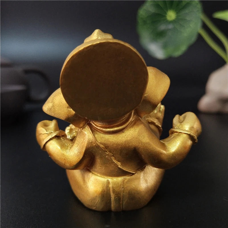 Handcrafted golden Buddha statue with a large circular head and arms resting on a dark surface.