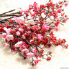 Branches of artificial silk cherry blossoms in shades of pink and red on a white fluffy background