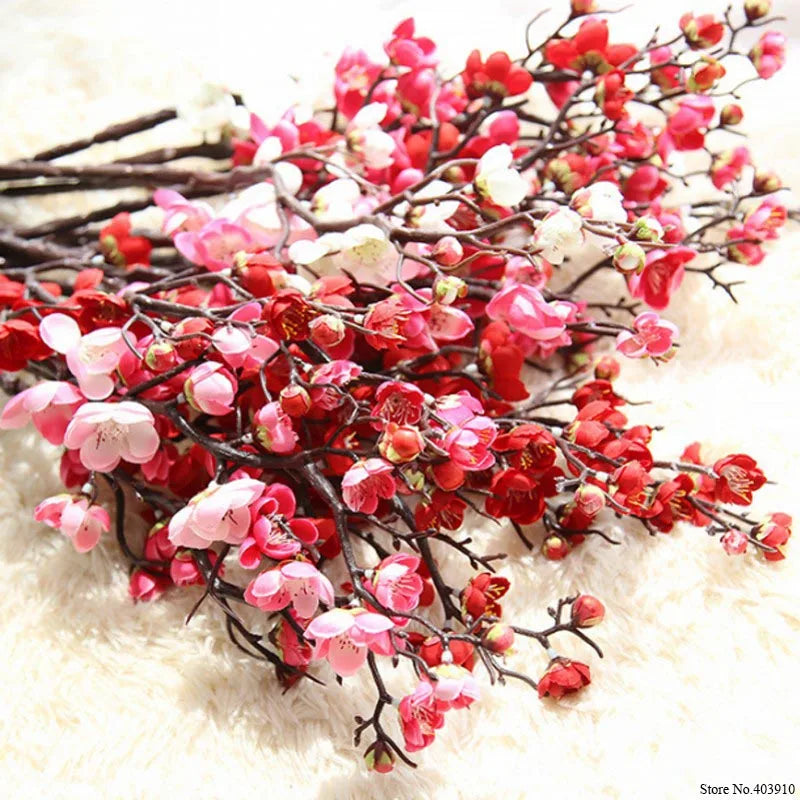 Branches of artificial silk cherry blossoms in shades of pink and red on a white fluffy background