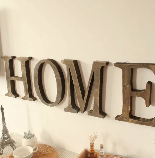 A row of rustic wooden alphabet letters spelling HOME mounted on a white wall.