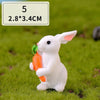 A white miniature rabbit figurine holding a carrot, placed on green grass.