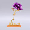 A gold foil artificial rose with a delicate stem and the word love on a small base.