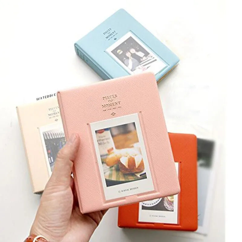 A hand holds a pink compact photo album for instant film next to a light blue album.