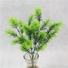 A vibrant green artificial fern plant with delicate fronds displayed in a glass vase.