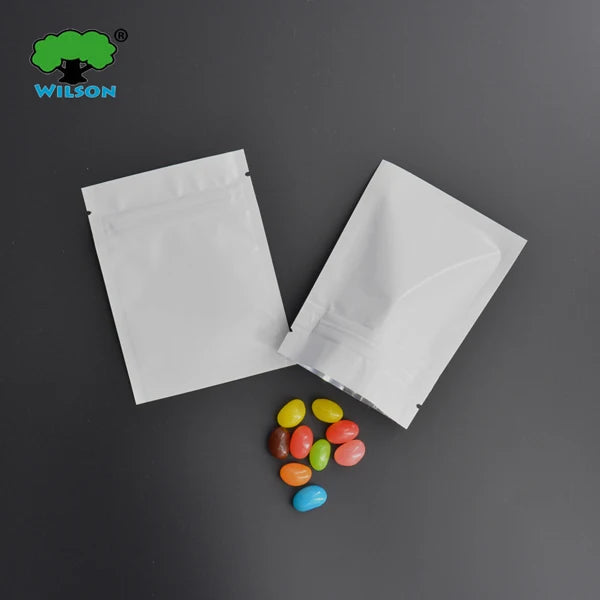 White foil zip bags containing colorful pills or candies are displayed on a dark surface.