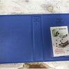 A blue compact photo album titled Pieces of Moment for instant film is shown on a wooden surface.