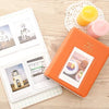 An orange compact photo album with a clear window displaying instant film photos and a yellow candle.