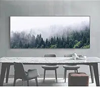 A long marble table with chairs in front of a large framed photograph of a misty forest.