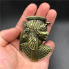 Une main tient un aimant réfrigérateur décoratif en métal représentant un profil de femme égyptienne antique en bronze olive.