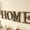 A row of rustic wooden alphabet letters spelling HOME mounted on a white wall.