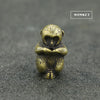 A small brass statue of a monkey with a face and hands, resting on a dark gray surface.