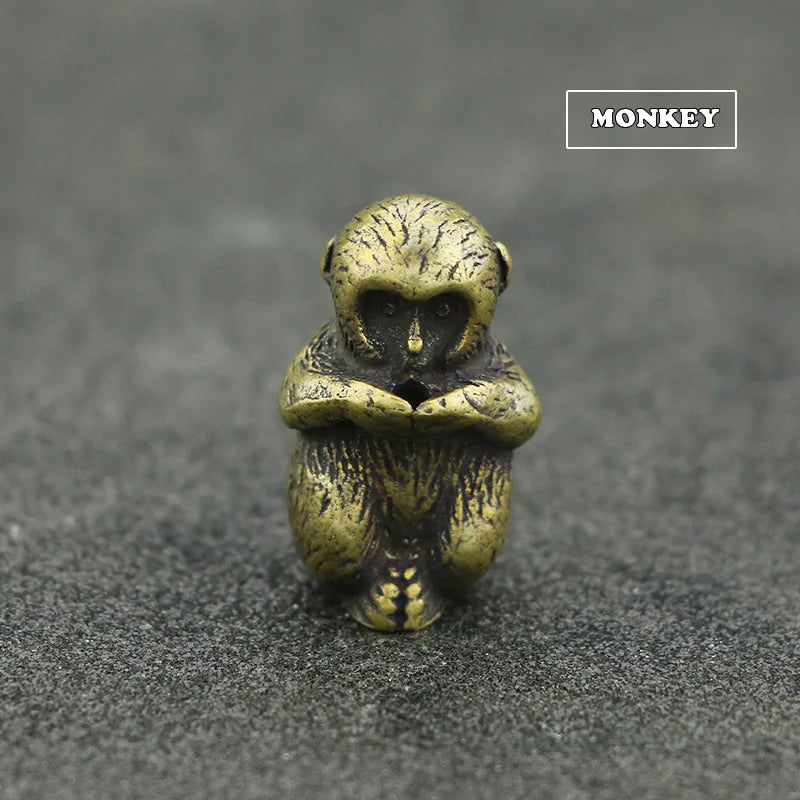 A small brass statue of a monkey with a face and hands, resting on a dark gray surface.