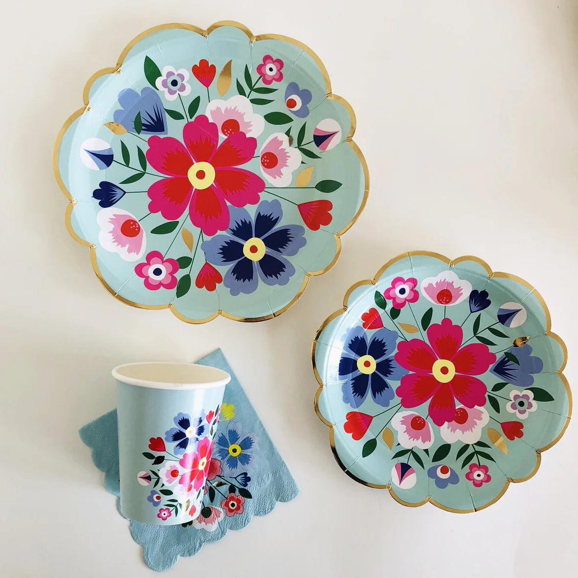A teal floral plate and matching paper cup set with pink, purple, and green flowers.