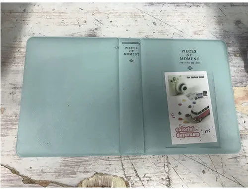 A light blue compact photo album with a clear cover and a section for instant film photos.