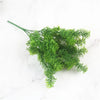 A sprig of bright green artificial fern leaves on a white marble background.