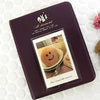 A dark purple compact photo album with a gold embossed design featuring a smiling face illustration.